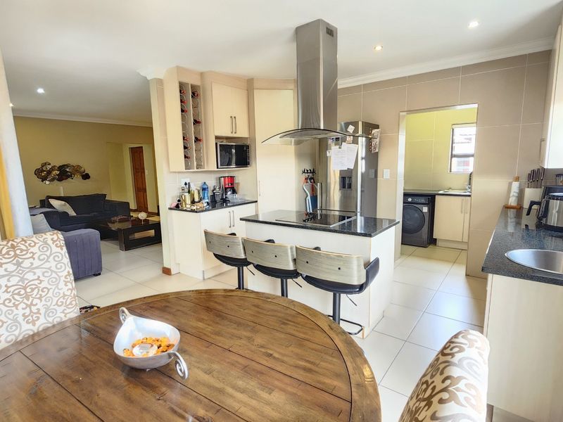 Open-plan kitchen featuring a central island with hob, granite countertops, ample cabinetry, and an adjoining scullery area, flowing into the living space.