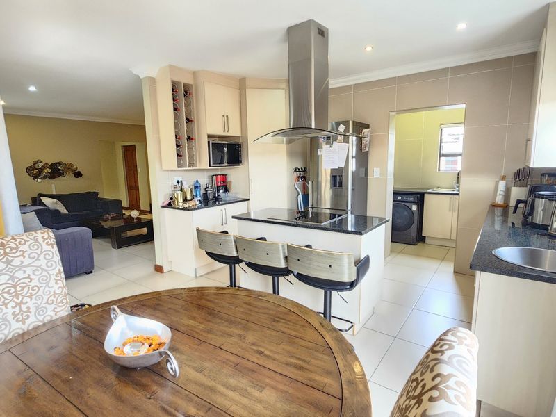 Spacious open-plan kitchen and living area featuring a central island with hob, modern cabinetry, granite countertops, and an adjoining scullery.