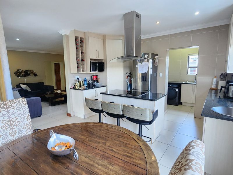 Spacious open-plan kitchen featuring a central island with granite countertops, modern cabinetry, and an adjoining scullery area, seamlessly flowing into the living space.