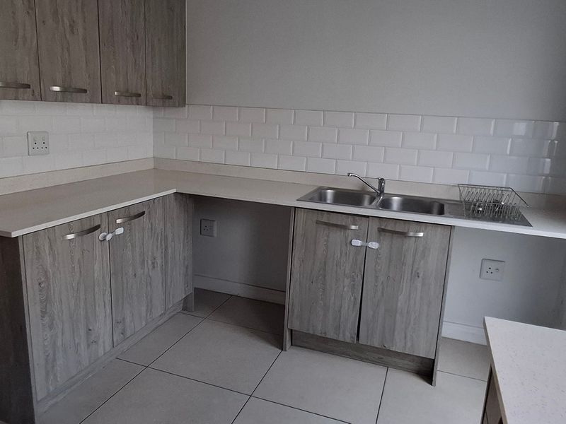 A functional kitchen featuring wood-look laminate cabinetry, a white subway tile backsplash, and a double bowl stainless steel sink with ample counter space.