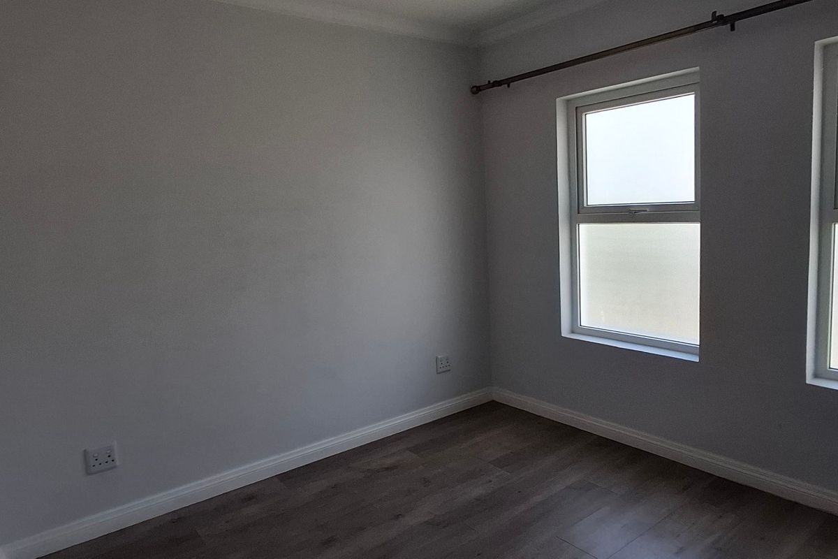 A bright, empty bedroom featuring modern laminate flooring, neutral walls, and dual windows with a fitted curtain rod.