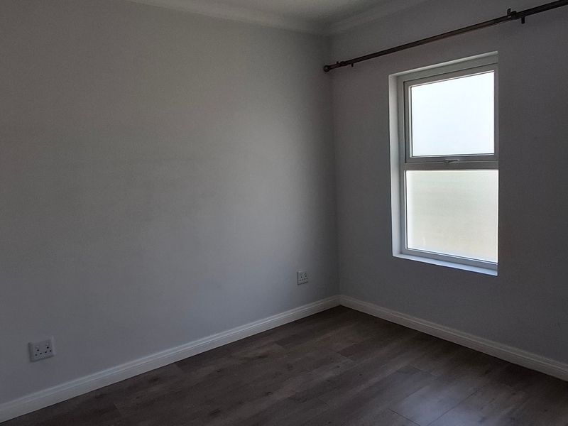 A bright, empty bedroom featuring modern laminate flooring, neutral walls, and dual windows with a fitted curtain rod.