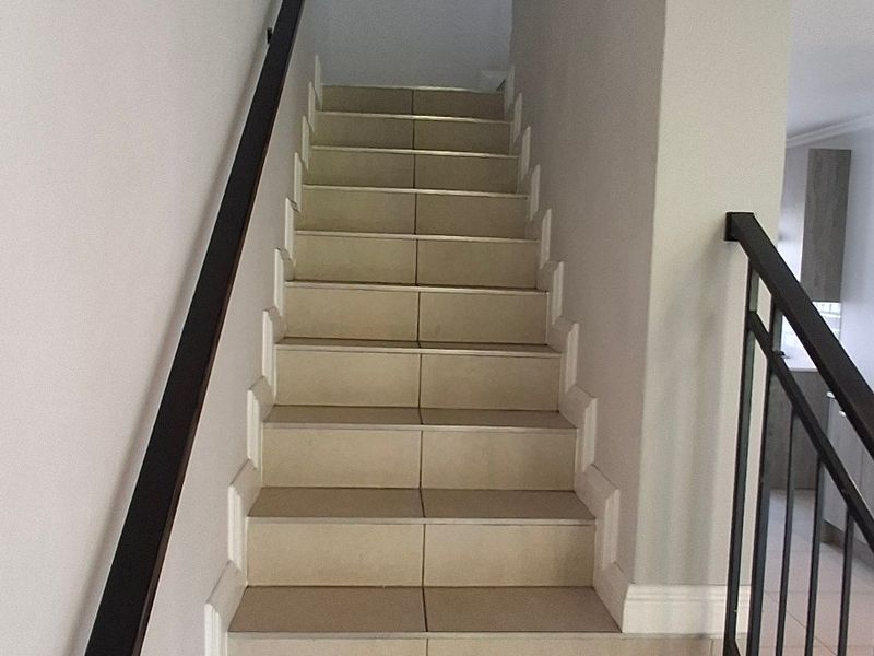 A clean, modern staircase featuring neutral floor tiles, a black metal balustrade, and a matching handrail, leading to the upper level of the townhouse.