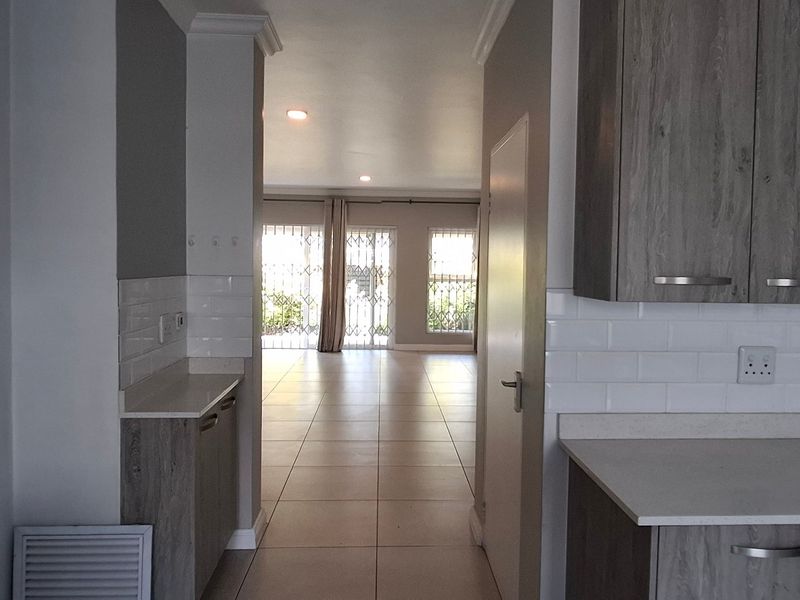 Open plan kitchen area featuring modern grey cabinetry, subway tile backsplash, and stone countertops, leading into a bright, tiled living space with security gates.