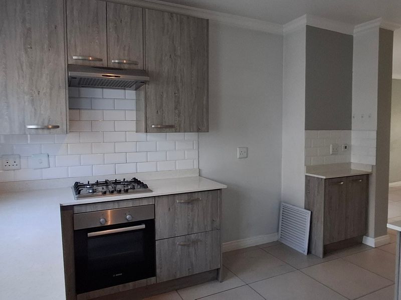 Modern kitchen featuring wood-look cabinetry, stone countertops, subway tile backsplash, and integrated gas hob with oven.