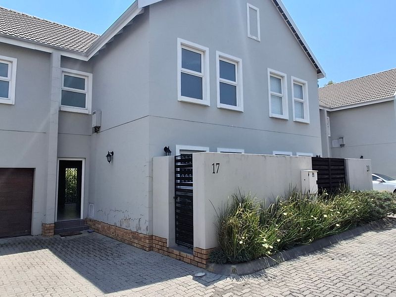 Front exterior view of a townhouse featuring a paved driveway, single garage, and a low-maintenance garden bed along the boundary wall.