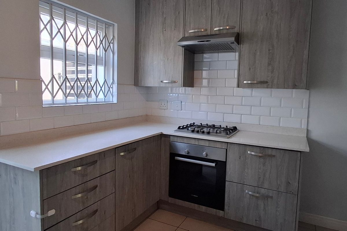 A modern kitchen featuring wood-look cabinetry, a gas hob, built-in oven, extractor fan, and a clean subway tile backsplash.