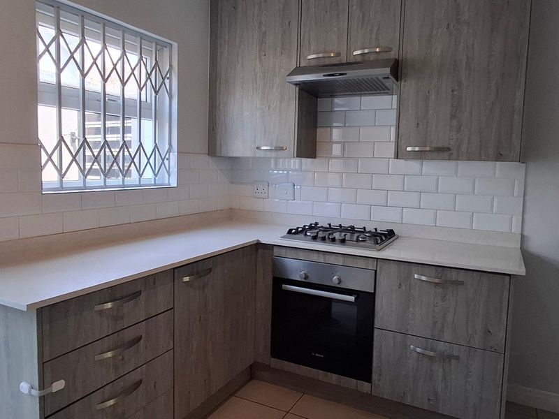 A modern kitchen featuring wood-look cabinetry, a gas hob, built-in oven, extractor fan, and a clean subway tile backsplash.