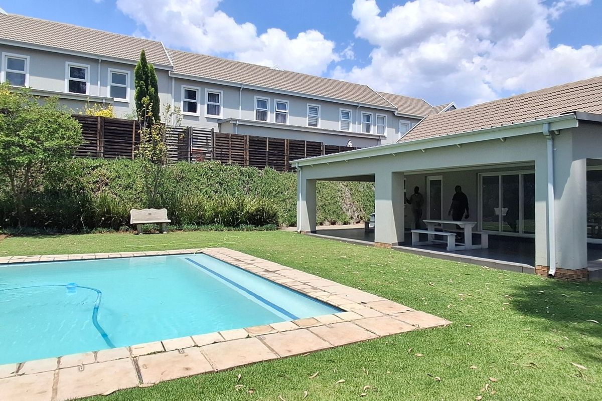 Rear exterior view of the townhouse featuring a private swimming pool, a covered patio area, and a well-maintained garden with a retaining wall.