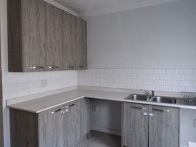 A functional kitchen featuring modern grey laminate cabinetry, a white subway tile backsplash, and a double bowl stainless steel sink with stone countertops.