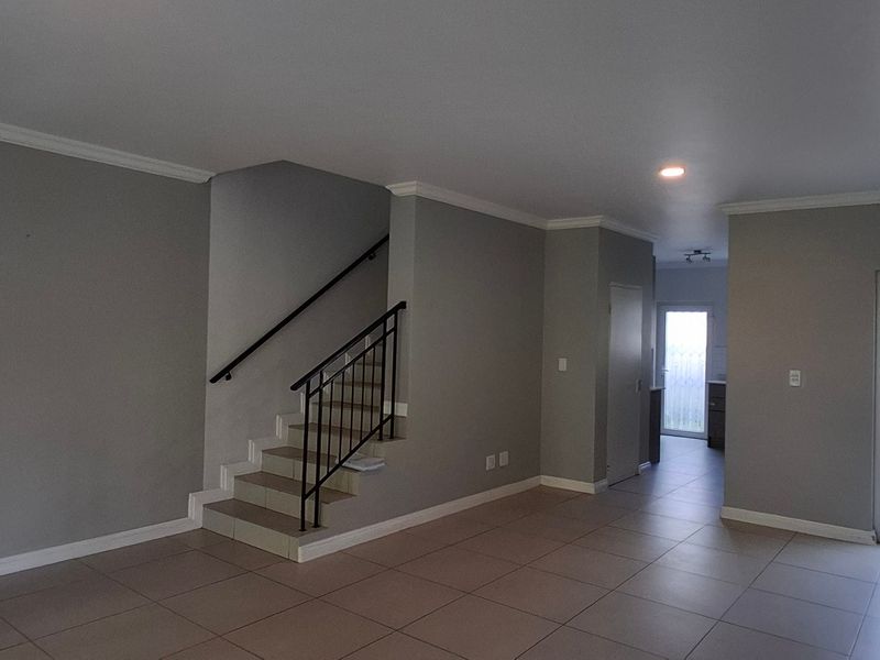 Spacious open-plan living area featuring tiled flooring, a central staircase with metal balustrade, and direct access to exterior doors.