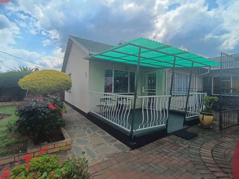 Rear view of the house featuring a covered patio area with security gates, paved walkways, and a well-maintained garden.