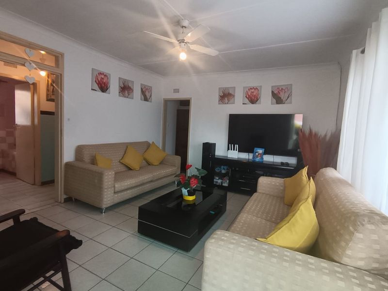 A comfortable living room featuring tiled flooring, a ceiling fan, and coved cornicing, providing a functional and well-lit space for relaxation.