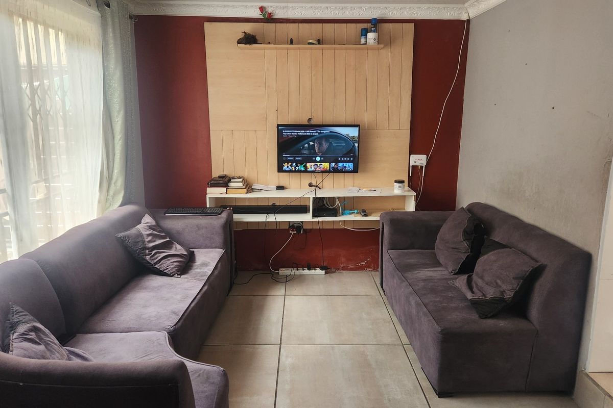 A living room featuring tiled flooring, a built-in media wall unit, and access to an outdoor area through a sliding glass door.