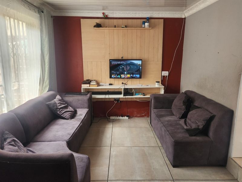 A living room featuring tiled flooring, a built-in media wall unit, and access to an outdoor area through a sliding glass door.