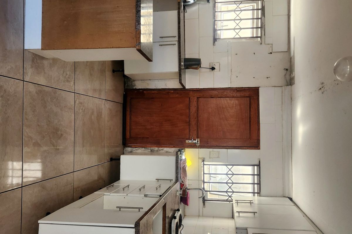 A functional kitchen featuring white cabinetry, tiled backsplash, and tiled flooring, requiring cosmetic updates to improve its overall condition and aesthetic appeal.