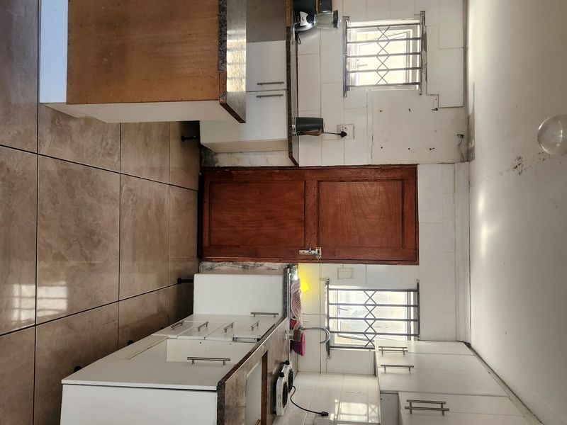 A functional kitchen featuring white cabinetry, tiled backsplash, and tiled flooring, requiring cosmetic updates to improve its overall condition and aesthetic appeal.