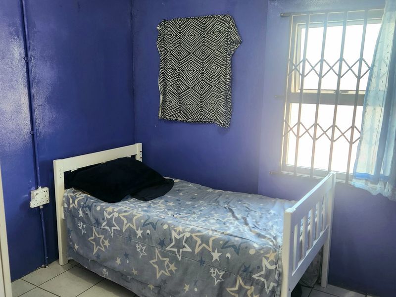A compact bedroom featuring tiled flooring, security bars on the window, and surface-mounted electrical conduit, requiring cosmetic updates to improve the overall aesthetic.