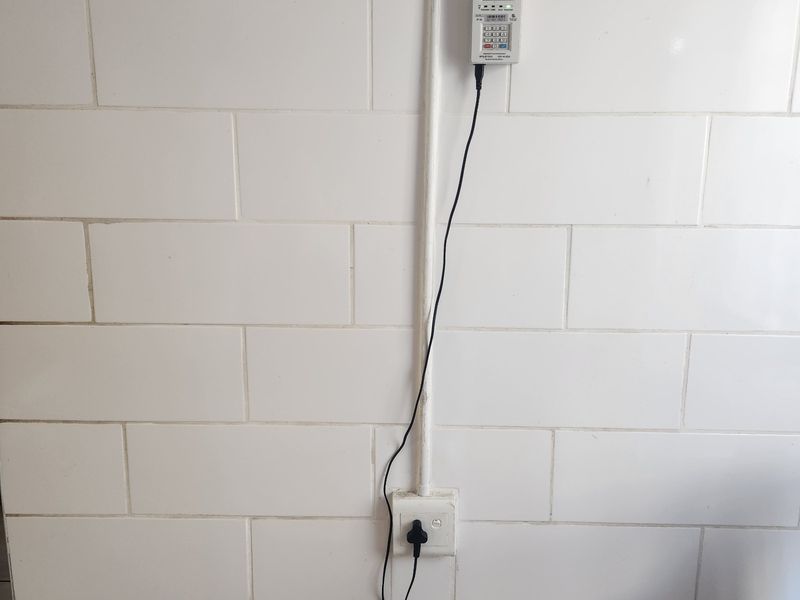 A utility wall featuring a mounted prepaid electricity meter with surface-mounted conduit and a standard electrical outlet.