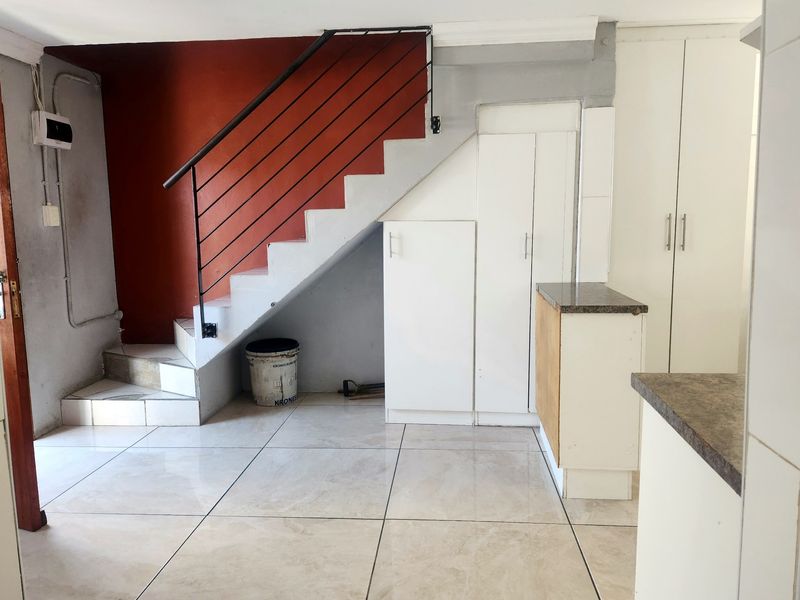 An open-plan living area featuring a staircase with a metal handrail, built-in storage cabinetry, and tiled flooring, offering potential for modernization.