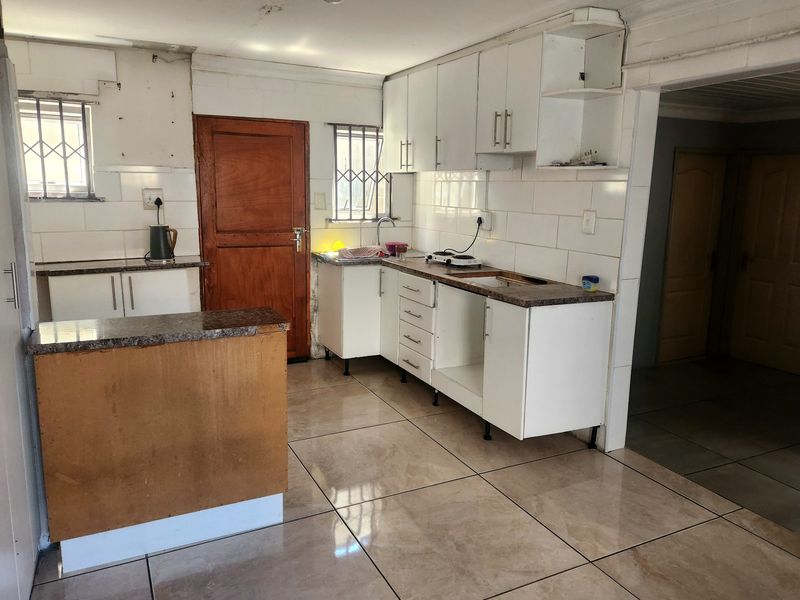 A functional kitchen featuring tiled flooring, granite countertops, and white cabinetry, currently requiring cosmetic updates and repairs to the cabinetry and ceiling.