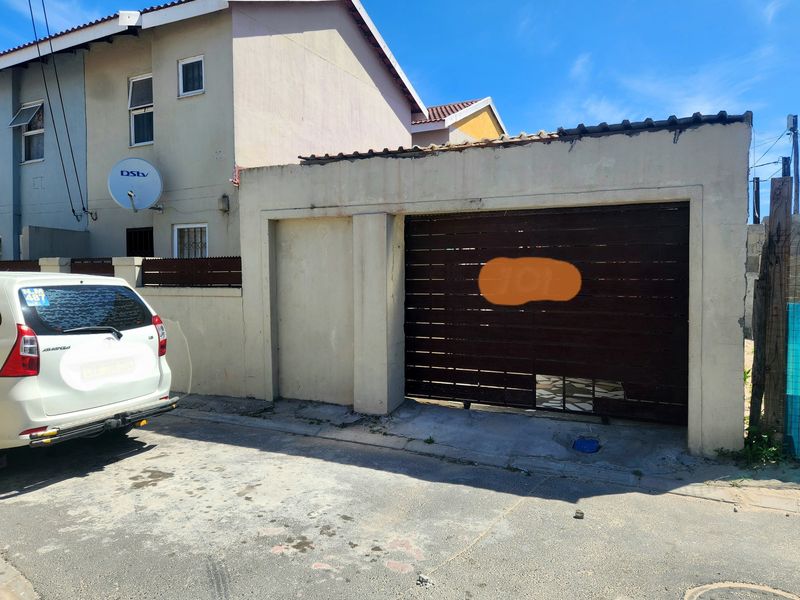 Front exterior view of the property featuring a garage with a damaged door and a boundary wall.