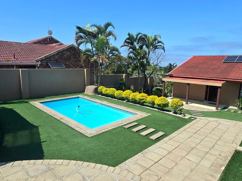 A well-maintained outdoor area featuring a swimming pool, paved patio, artificial lawn, and solar panels on the roof.