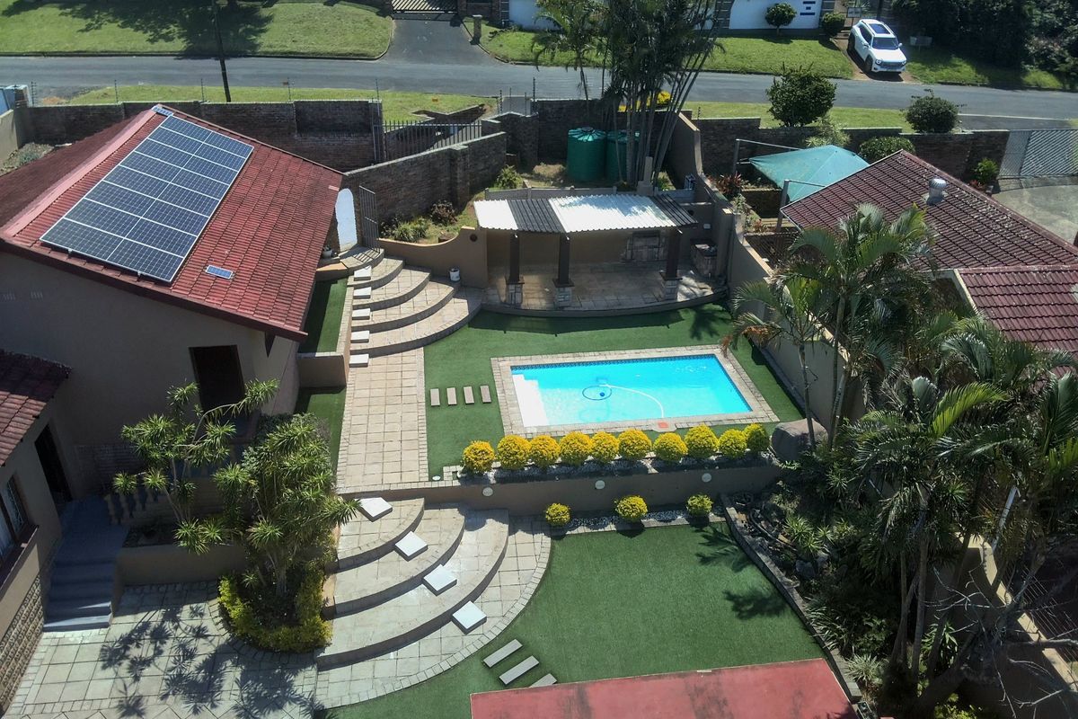 Aerial view of a residential property featuring a swimming pool, covered patio area, landscaped garden, and solar panels installed on the tiled roof.
