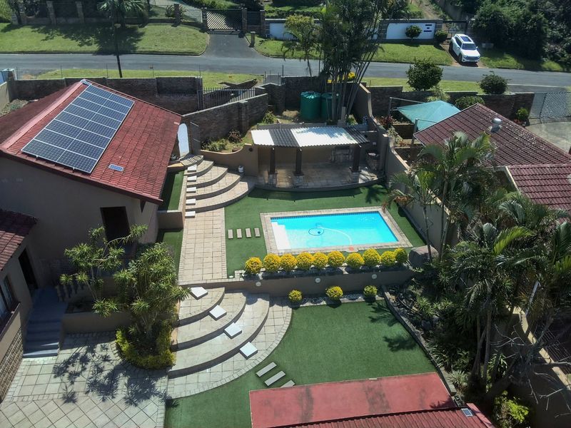 Aerial view of a residential property featuring a swimming pool, covered patio area, landscaped garden, and solar panels installed on the tiled roof.
