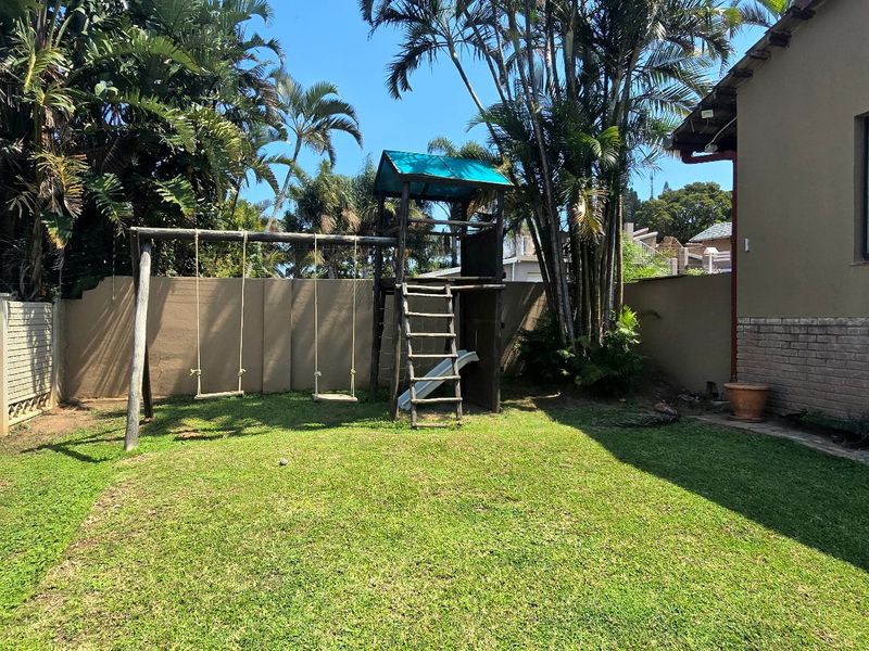 A private rear garden featuring a well-maintained lawn, brick boundary walls with electric fencing, and established palm trees.