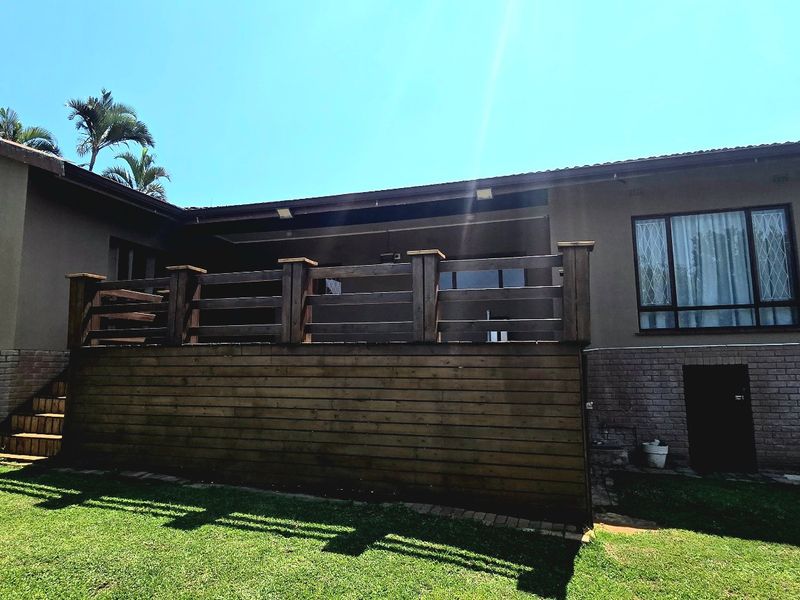 Rear view of the property featuring a raised timber deck, brick and plaster facade, and a well-maintained lawn area.