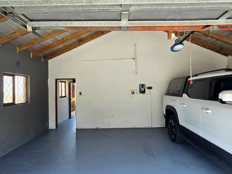 A functional garage space featuring exposed timber roof trusses, painted concrete flooring, and a sectional garage door with direct access to the home.