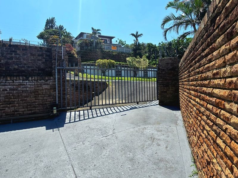 Front entrance view featuring a concrete driveway, brick boundary walls, and a metal security gate leading to the property.