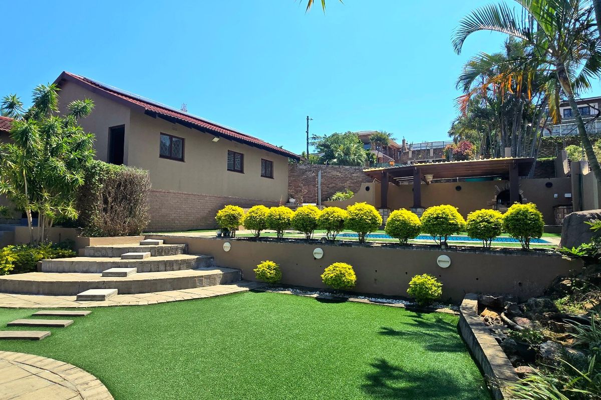 A well-maintained rear garden featuring a swimming pool, tiered retaining walls, paved patio areas, and a built-in braai, perfect for outdoor entertaining.