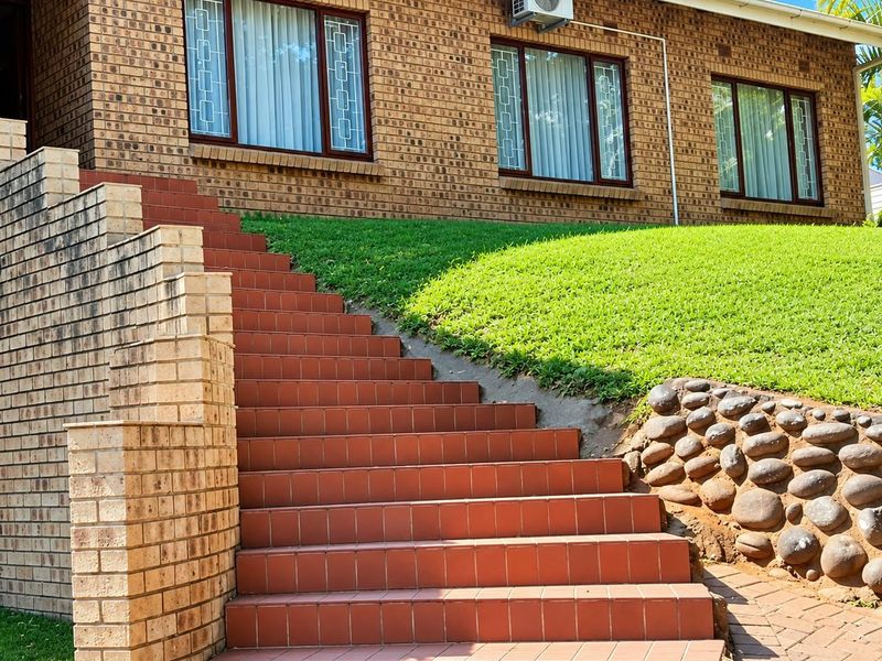 Front exterior view featuring a face brick facade, a tiled staircase leading to the entrance, and a landscaped garden with a stone-retaining feature.
