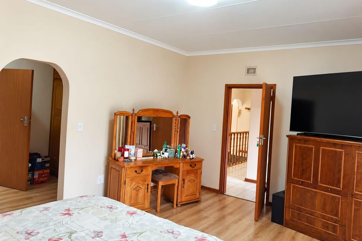 A spacious bedroom featuring light-toned laminate flooring, a classic archway entrance, and neutral wall finishes, offering a comfortable and functional living space.