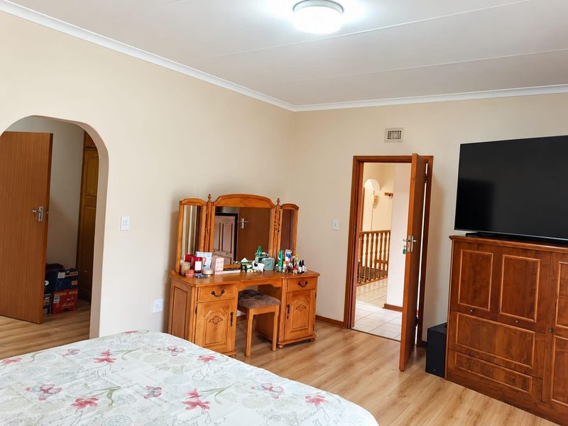 A spacious bedroom featuring light-toned laminate flooring, a classic archway entrance, and neutral wall finishes, offering a comfortable and functional living space.