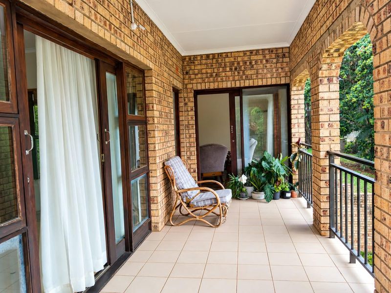 A covered patio featuring exposed brick walls, arched columns, tiled flooring, and sliding glass doors providing access to the interior living space.