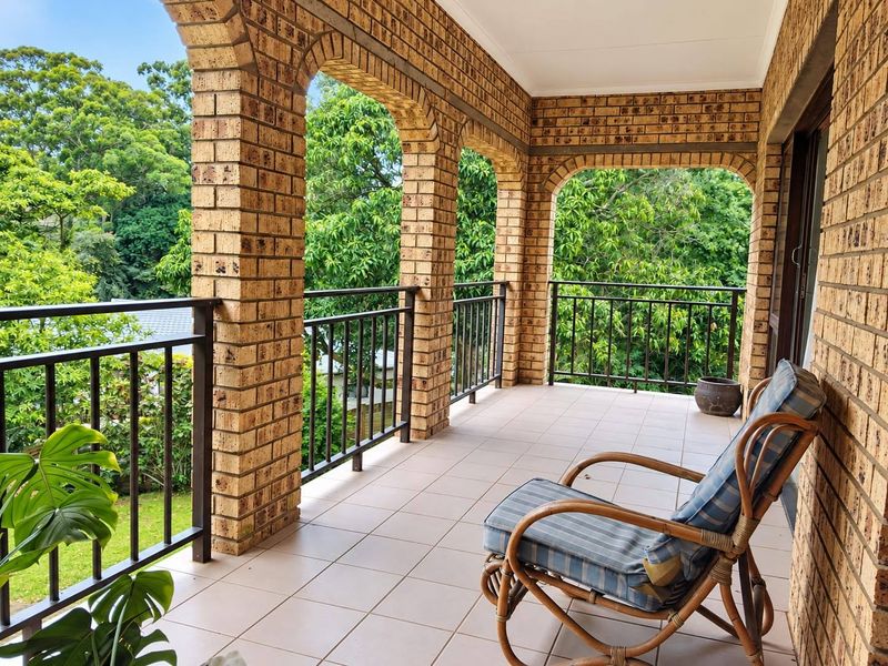 A covered balcony featuring classic brick arches, tiled flooring, and a metal balustrade, offering a pleasant outdoor space with garden views.