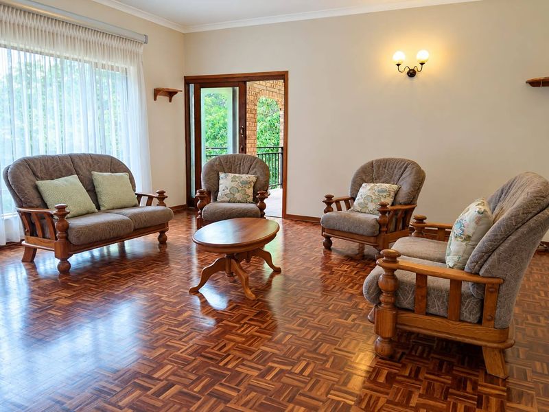 A spacious living room featuring polished parquet flooring, neutral walls, and a sliding glass door providing access to an outdoor patio area.
