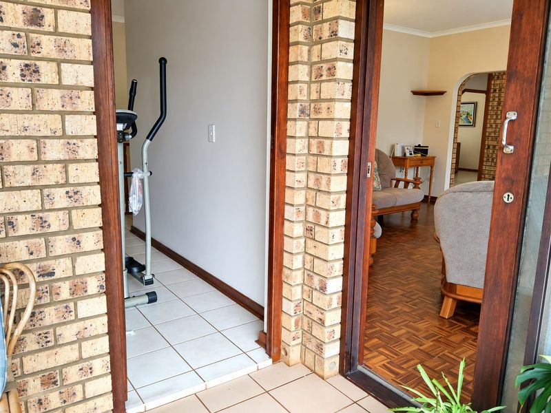 A view from a patio into a tiled hallway and adjacent living area featuring parquet flooring and exposed brick architectural details.