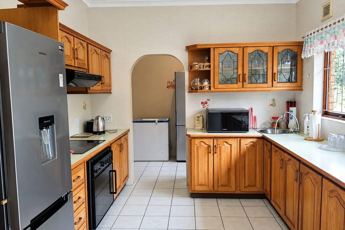 A functional kitchen featuring traditional wooden cabinetry, tiled flooring, a built-in oven, and an archway leading to a secondary utility or scullery area.