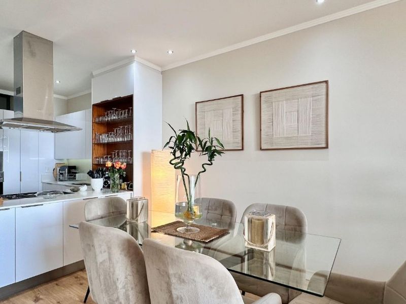 Modern open-plan kitchen and dining area featuring sleek white cabinetry, stainless steel extractor fan, and warm laminate flooring with recessed lighting.