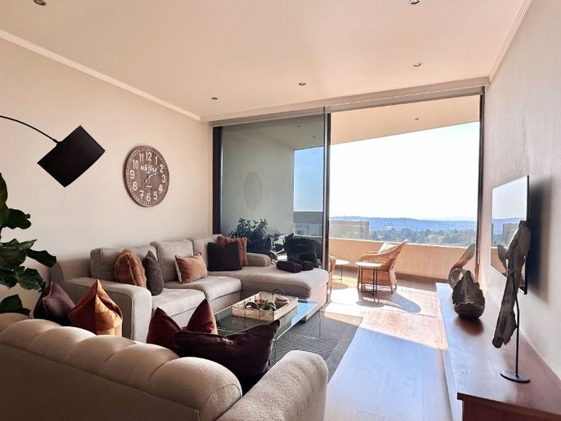 A bright living room featuring large sliding glass doors that open onto a balcony with expansive views and modern recessed lighting.