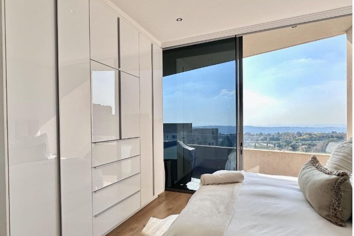 Modern bedroom featuring high-gloss built-in cupboards, recessed lighting, and a large sliding glass door opening to a balcony with expansive views.