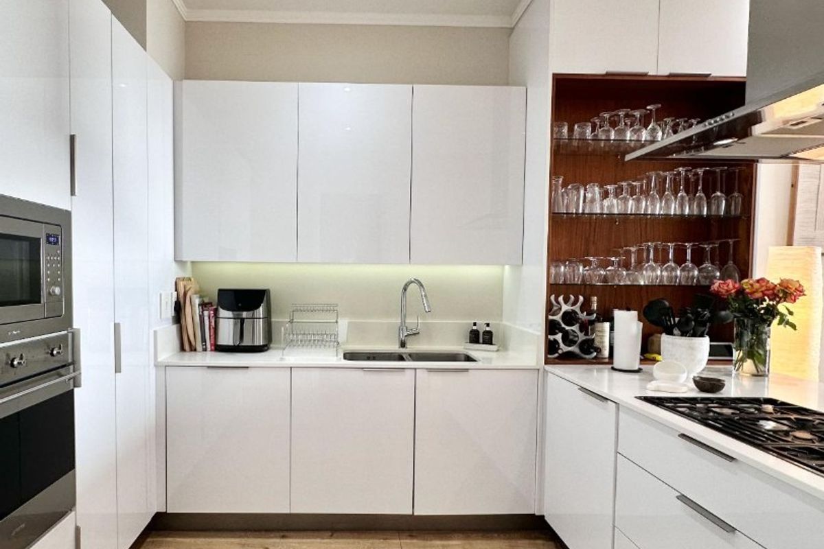 Modern kitchen featuring white gloss cabinetry, integrated appliances, gas hob, extractor fan, and stylish glass shelving with under-cabinet lighting.