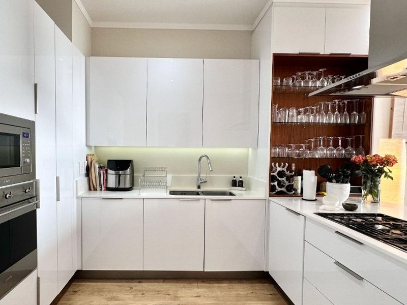 Modern kitchen featuring white gloss cabinetry, integrated appliances, gas hob, extractor fan, and stylish glass shelving with under-cabinet lighting.