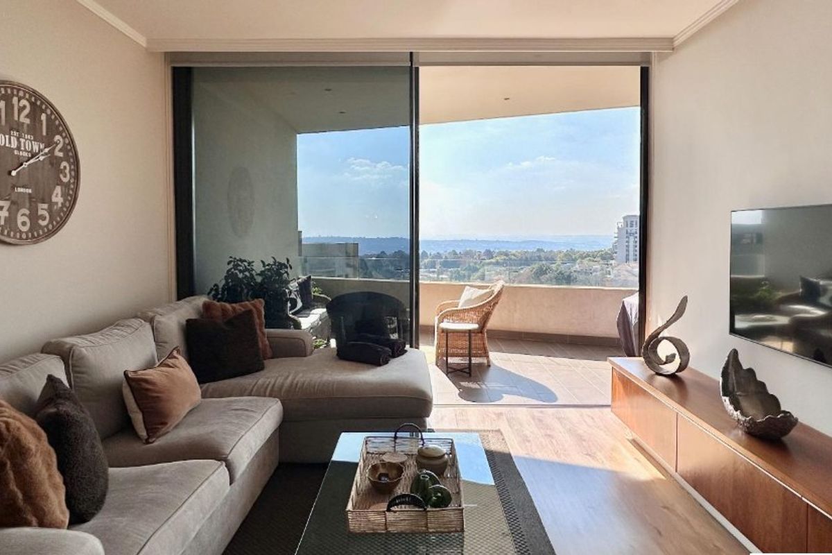 A bright living room featuring laminate flooring and large sliding glass doors that open onto a balcony with expansive views.