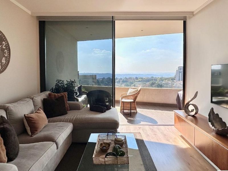 A bright living room featuring laminate flooring and large sliding glass doors that open onto a balcony with expansive views.