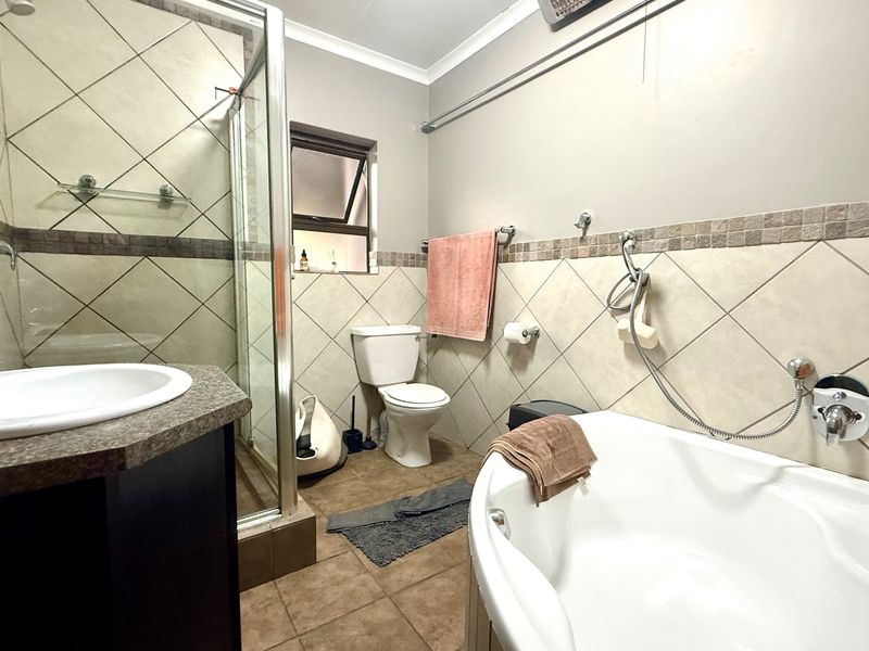 A functional bathroom featuring a separate shower enclosure, bathtub, vanity basin, and toilet with neutral wall and floor tiling.